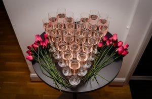 Champagne glasses arranged in a heart formation.  Filled with Rose prosecco and arranged on a black table with rose buds on either side